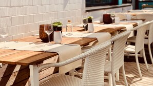 An outdoor dining area with wooden tables and white wicker chairs, set against a white brick wall. - Aqua Hotel (Konstanz)