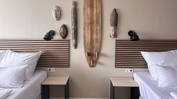 Une chambre d’hôtel moderne avec deux lits, des têtes de lit en bois et une planche de surf accrochée au mur.