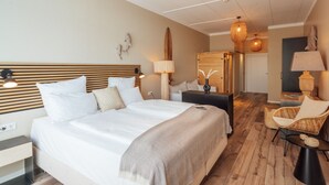 A hotel room with a large bed, a wooden headboard, a desk, a chair, and a small table. - Aqua Hotel (Konstanz)