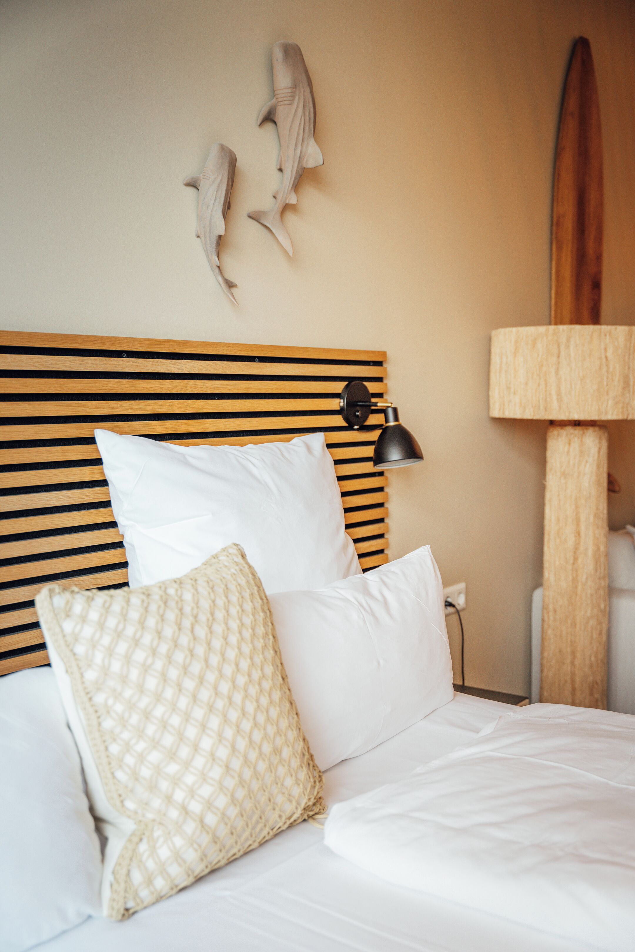 A bed with white bedding, a wooden headboard, and two decorative fish on the wall.