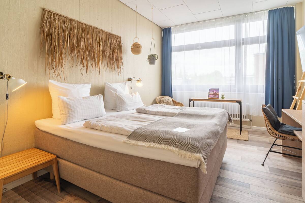 Ein helles Schlafzimmer mit einem großen Bett, Nachttischen, einem Sessel und einem kleinen Tisch mit einer Lampe.