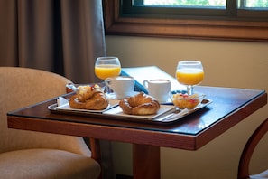 A breakfast tray with croissants, fruit, and two glasses of orange juice on a wooden table near a window. - Motel Jardin (Oleiros)