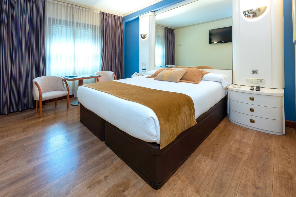 A hotel room with a large bed, a desk, a chair, and a wardrobe.