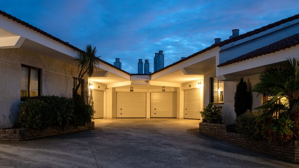 A gated parking area with two garage doors, surrounded by landscaping and a clear sky. - Motel Jardin (Oleiros)