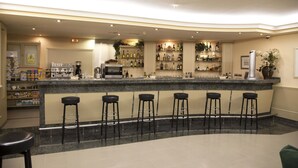 A bar area with a marble countertop, multiple stools, and shelves stocked with bottles. - Motel Jardin (Oleiros)