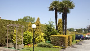 A well-maintained garden with a wooden pergola, neatly trimmed hedges, and a palm tree. - Motel Jardin (Oleiros)