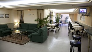 A hotel lobby with green sofas, a coffee table, a TV mounted on the wall, and a dining area with tables and chairs. - Motel Jardin (Oleiros)