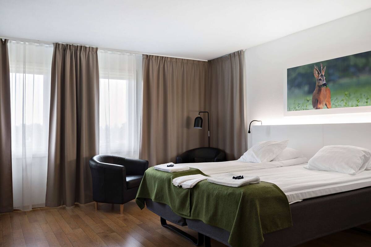 A hotel room with a bed, a chair, and a painting of a deer on the wall.