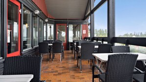 Eine Terrasse im Freien mit Korbstühlen und -stühlen, einer roten Tür und großen Fenstern.