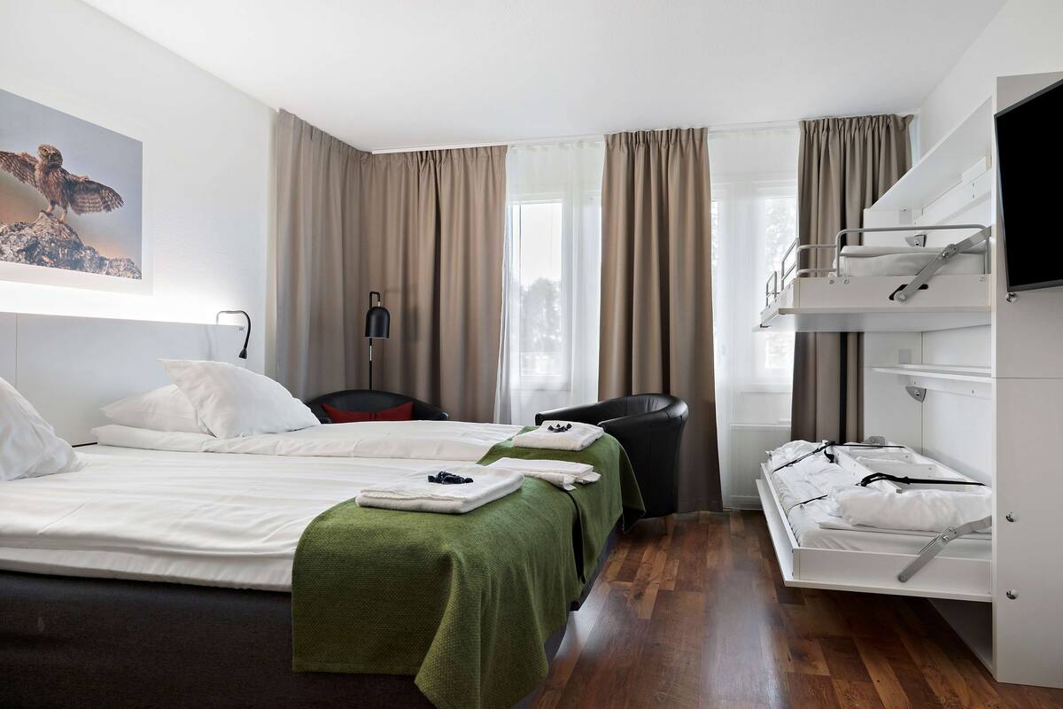 A hotel room with two beds, a desk, a chair, a TV, and a window with curtains.