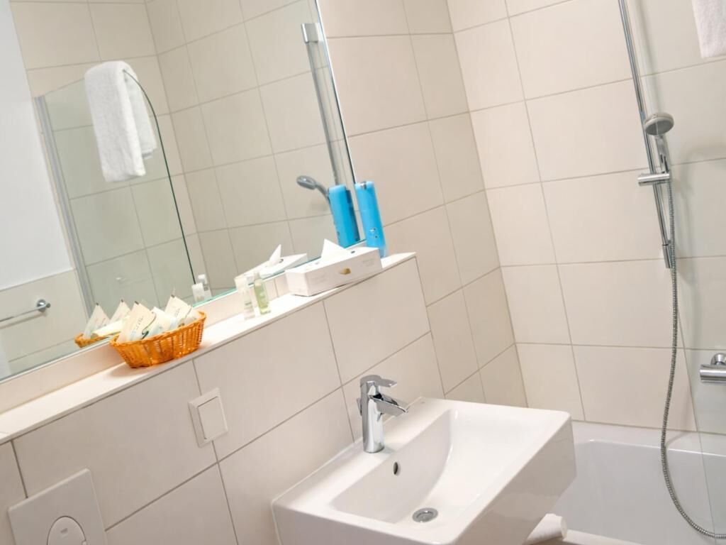 A bathroom with a white sink, a mirror, and a shower. There is a basket of toiletries on the counter.