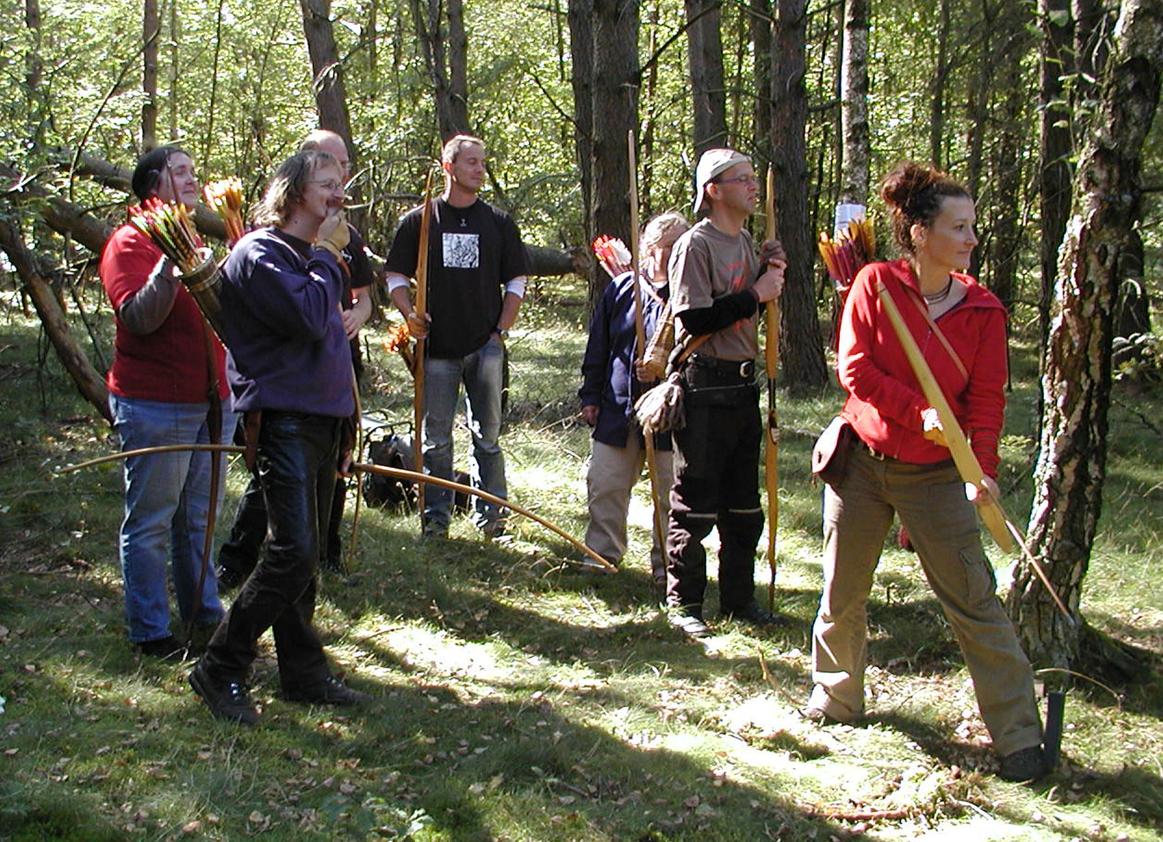 A group of people in a forested area, some holding bows and arrows.