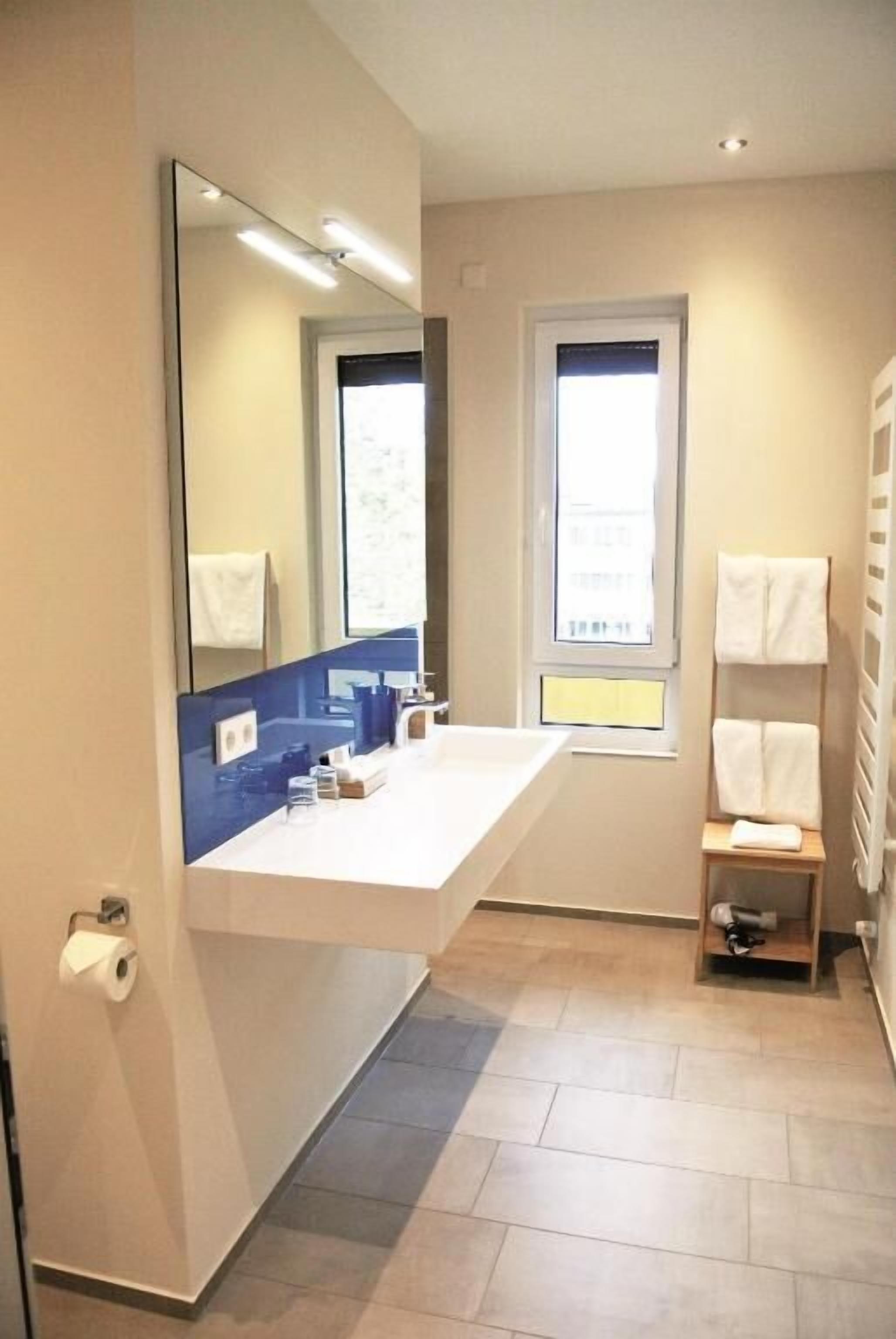 A modern bathroom with a large mirror, a white sink, and a towel rack.