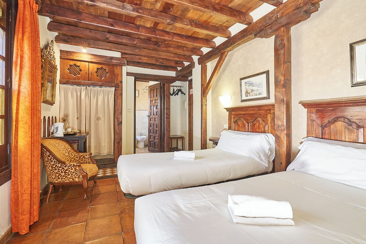 A room with two beds, wooden beams, a chair, and a wardrobe.