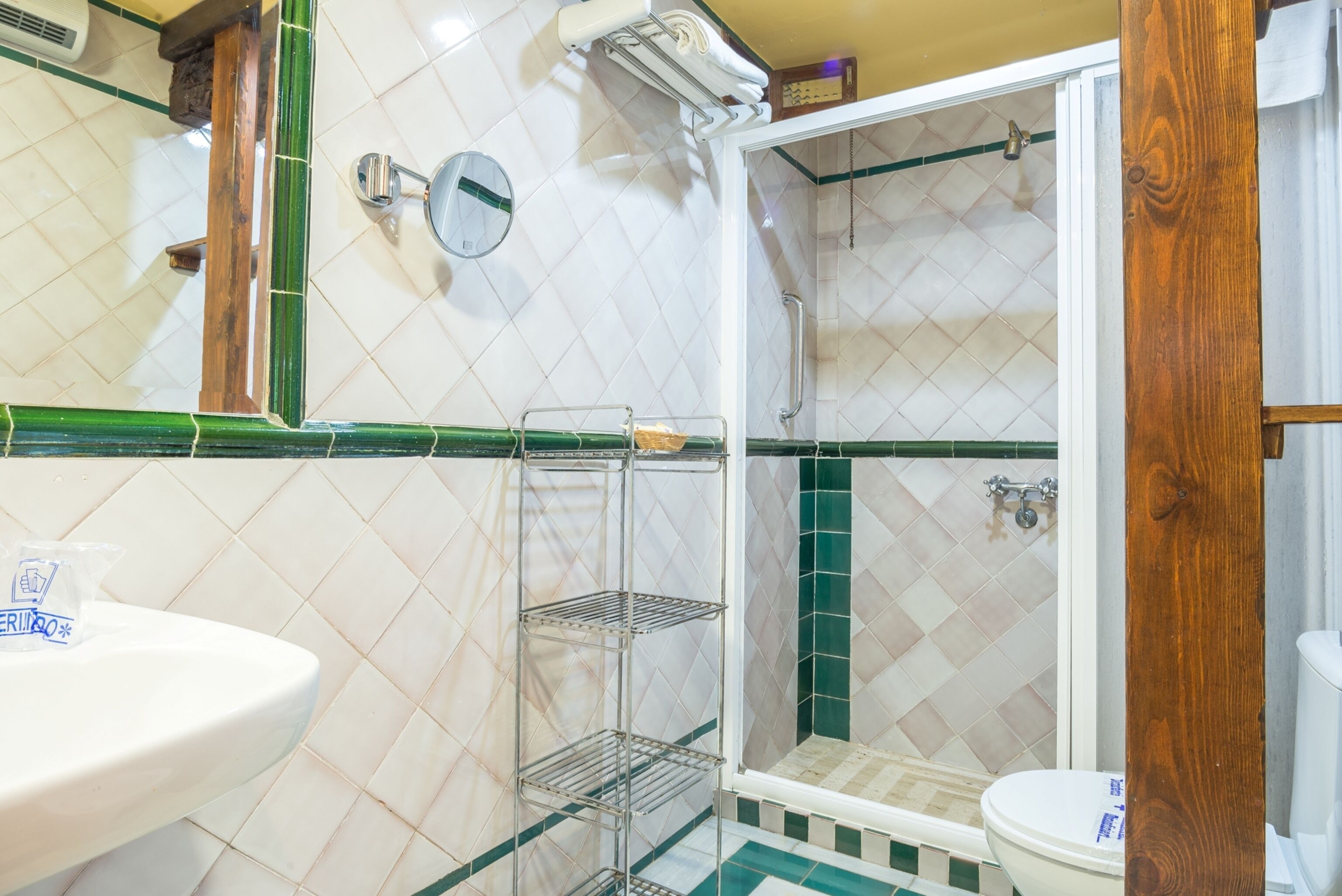 Un baño con lavamanos blanco, espejo, ducha con puerta de cristal y retrete.