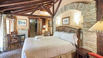 Habitación de hotel con una cama grande, vigas de madera en el techo, paredes de piedra, una mesita y una silla.