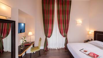 A hotel room with a bed, a desk with a chair, a lamp, and a nightstand with a phone.