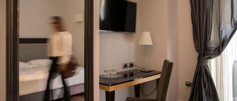 A hotel room with a bed, a desk with a lamp, a TV, and a chair.