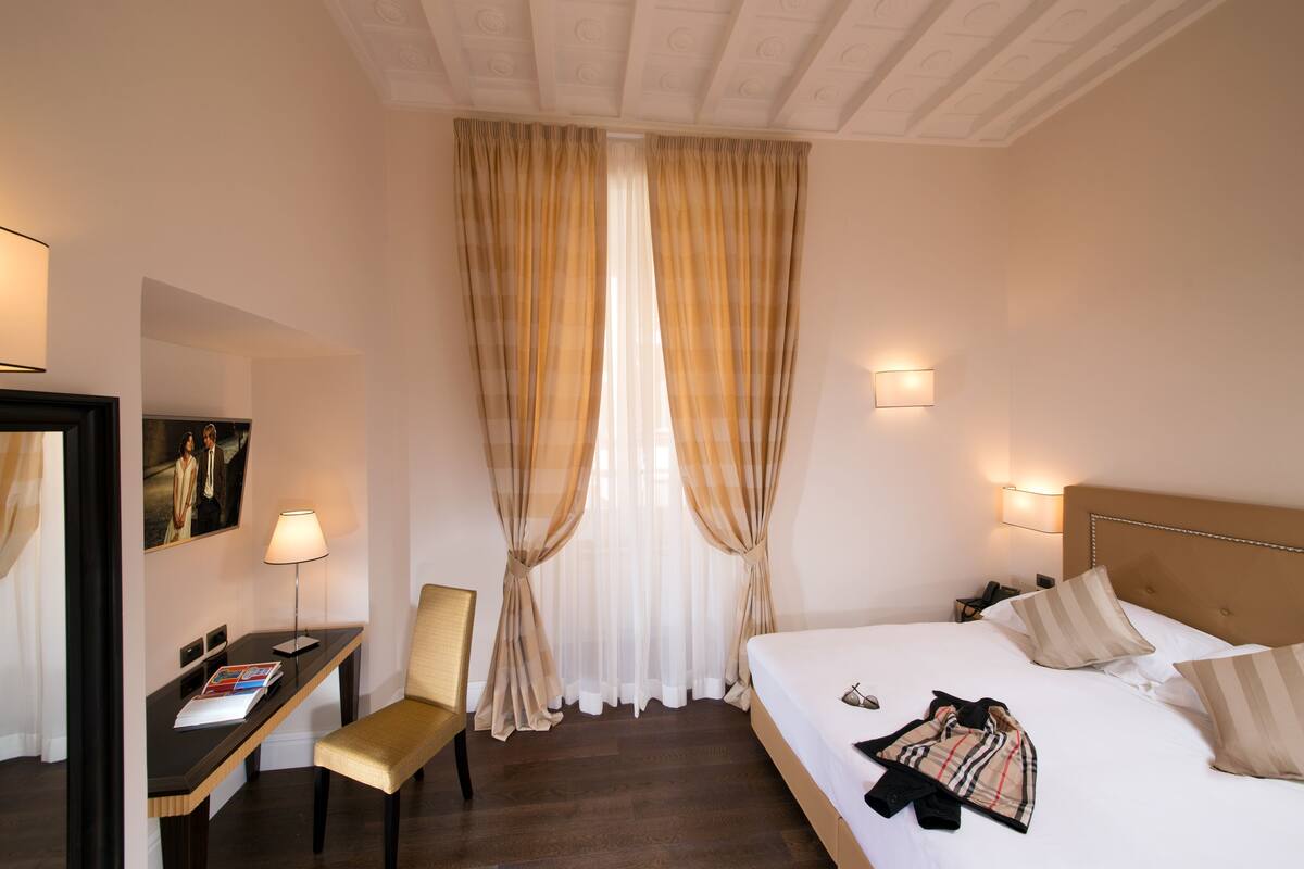 A hotel room with a bed, a desk with a chair, a lamp, and a picture on the wall.