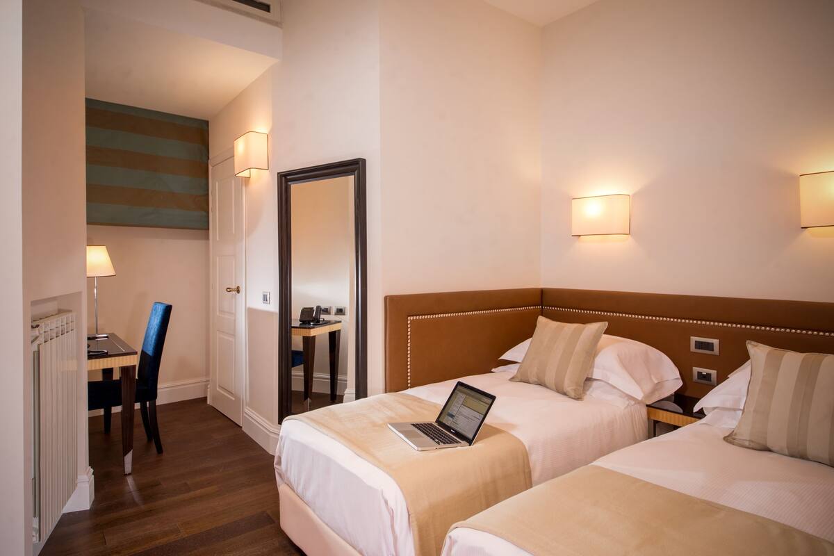 A hotel room with two beds, a desk, and a chair. There is a laptop on one bed.
