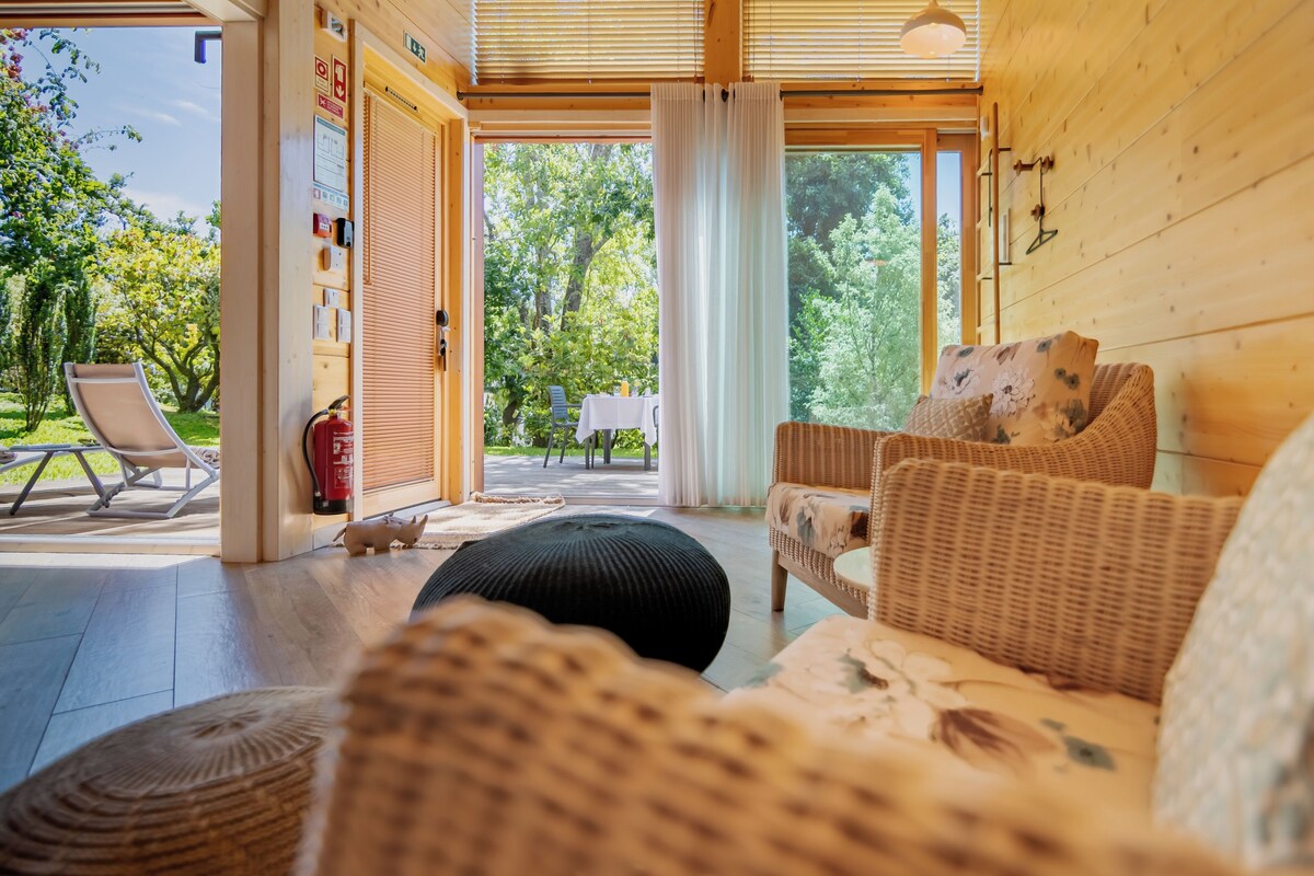 A cozy wooden interior with wicker furniture, a sliding glass door leading to an outdoor area with a table and chairs, and a fire extinguisher on the floor.