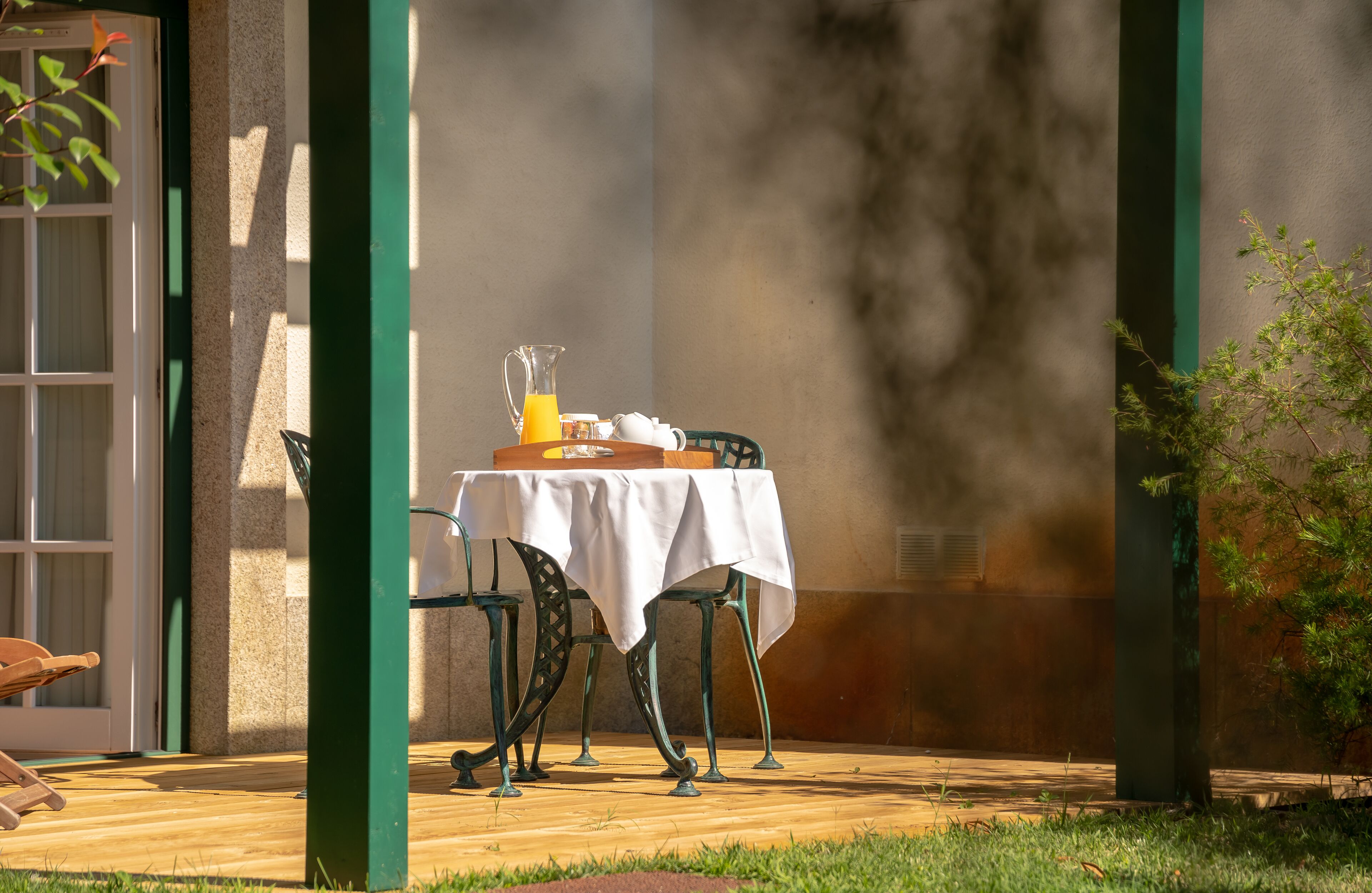 Un patio exterior con una mesa dispuesta para el desayuno, que incluye una jarra de jugo de naranja y una tetera.
