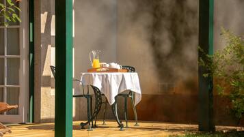 Un patio exterior con una mesa dispuesta para el desayuno, que incluye una jarra de jugo de naranja y una tetera.
