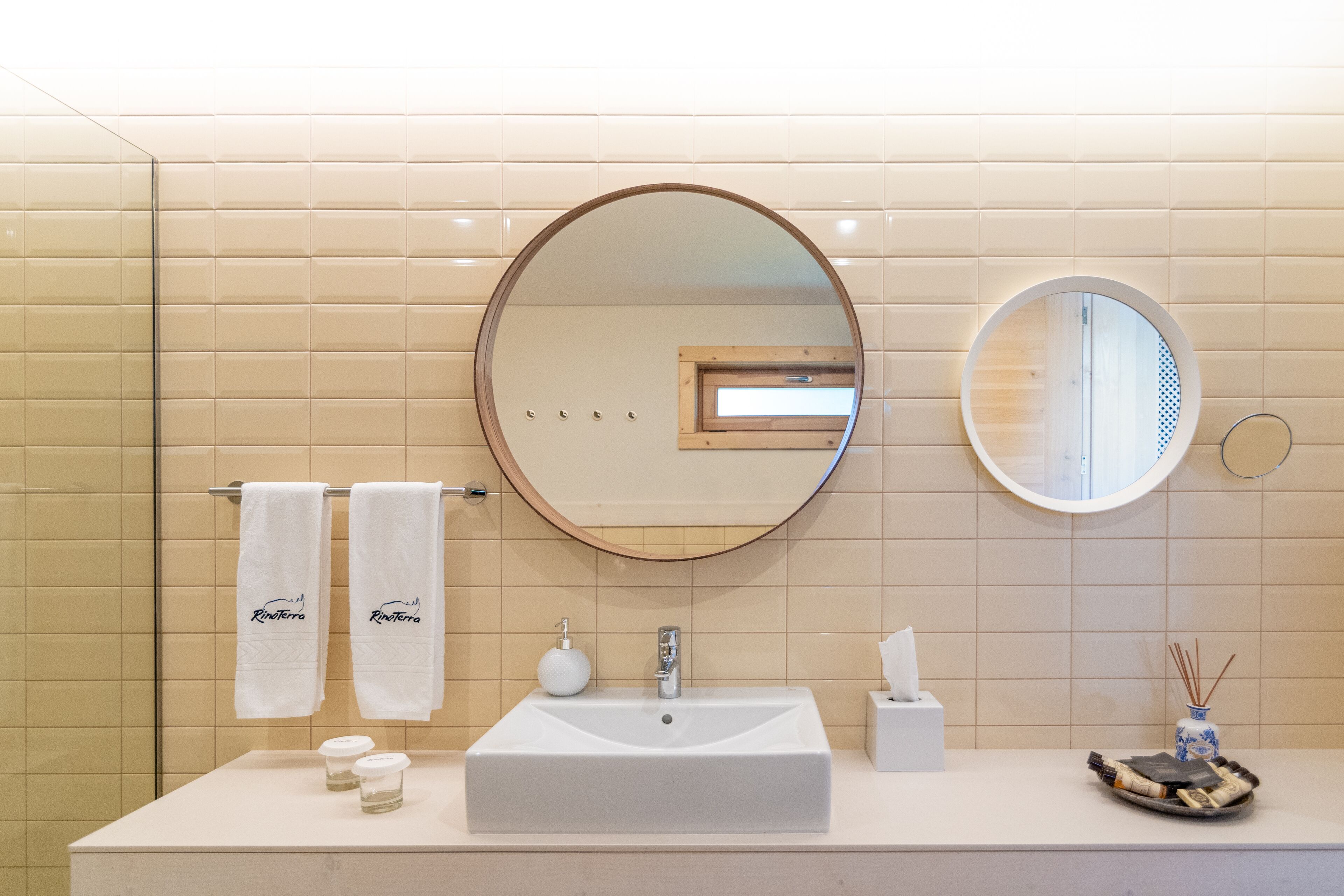 Un baño con un lavamanos grande y rectangular, dos espejos redondos y un perchero con dos toallas blancas.