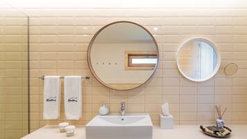 Un baño con un lavamanos grande y rectangular, dos espejos redondos y un perchero con dos toallas blancas.