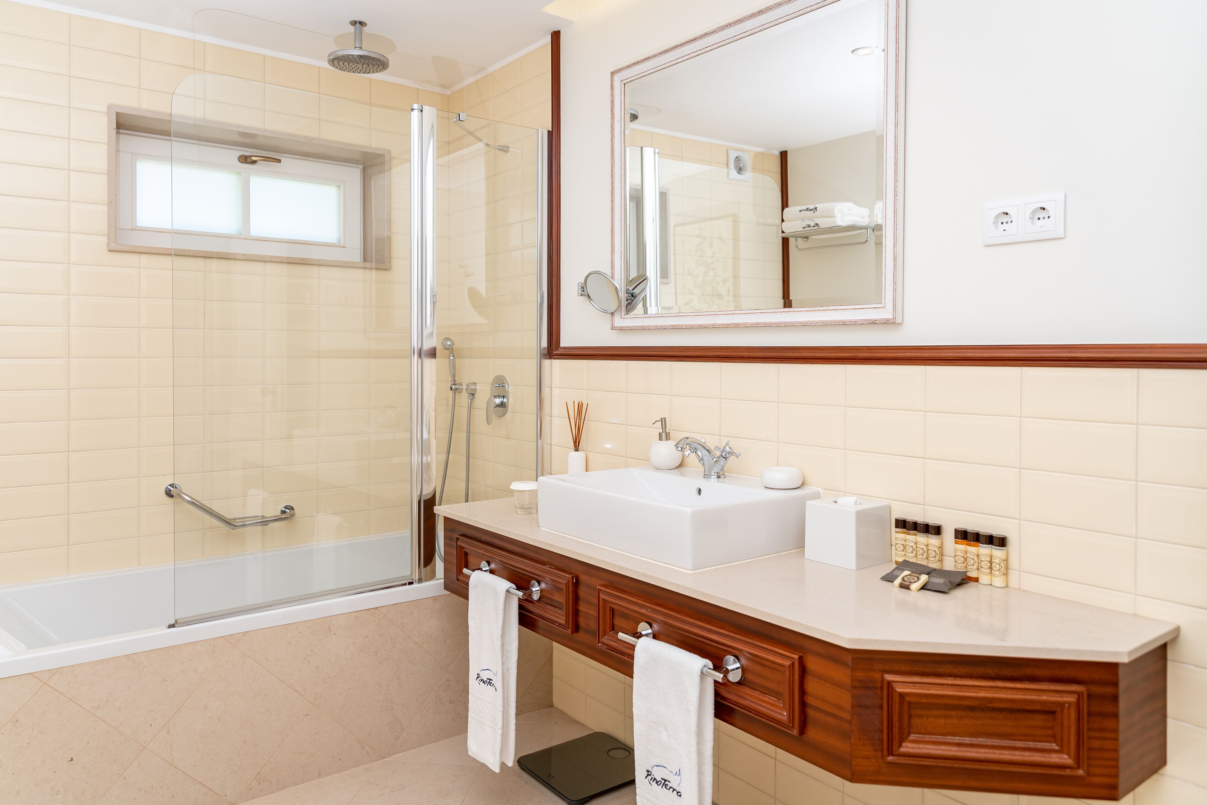 Un baño moderno con cabina de ducha de vidrio, un espejo grande, un lavabo blanco y muebles de madera.