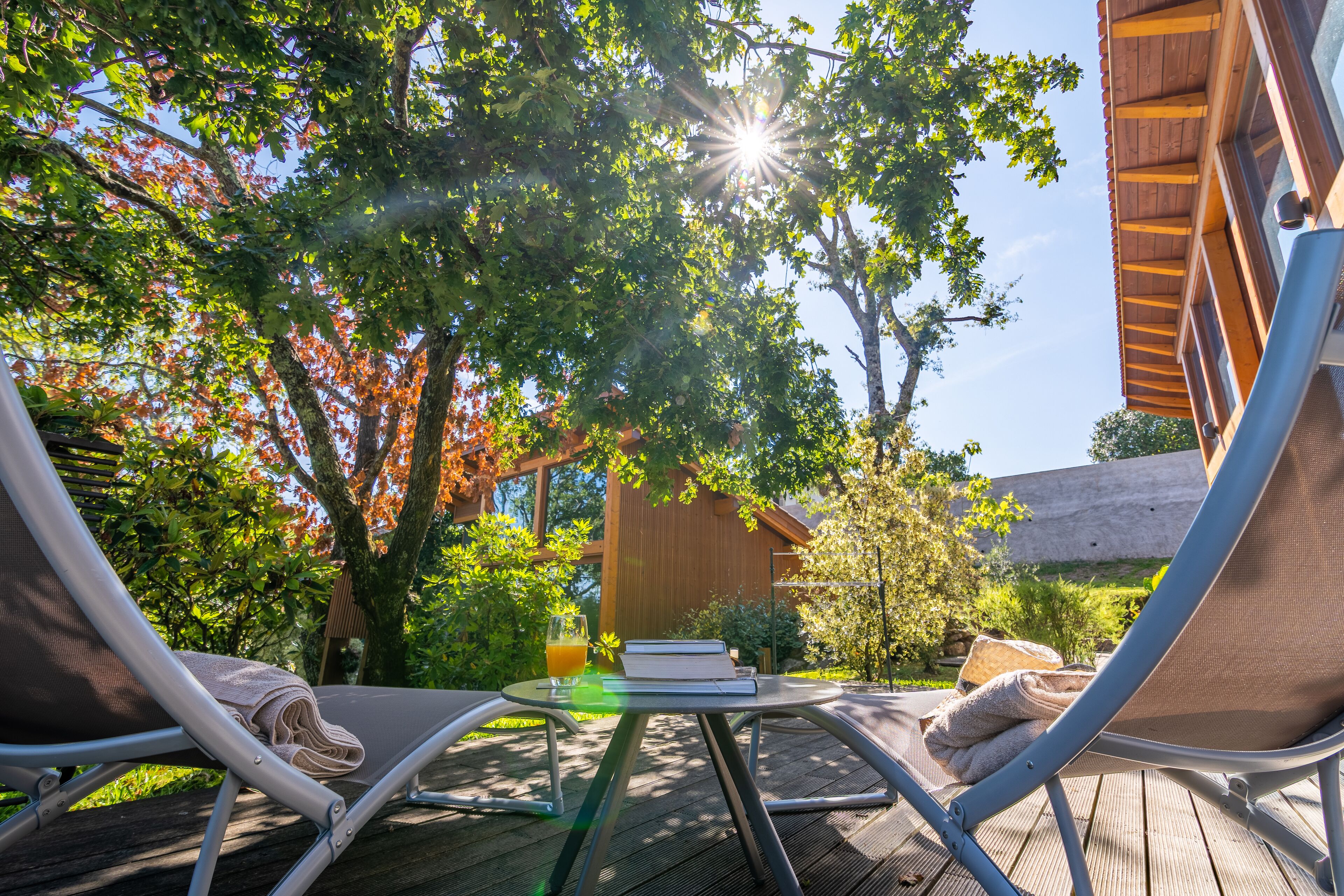 A sunlit outdoor seating area with a table, two lounge chairs, and a book.