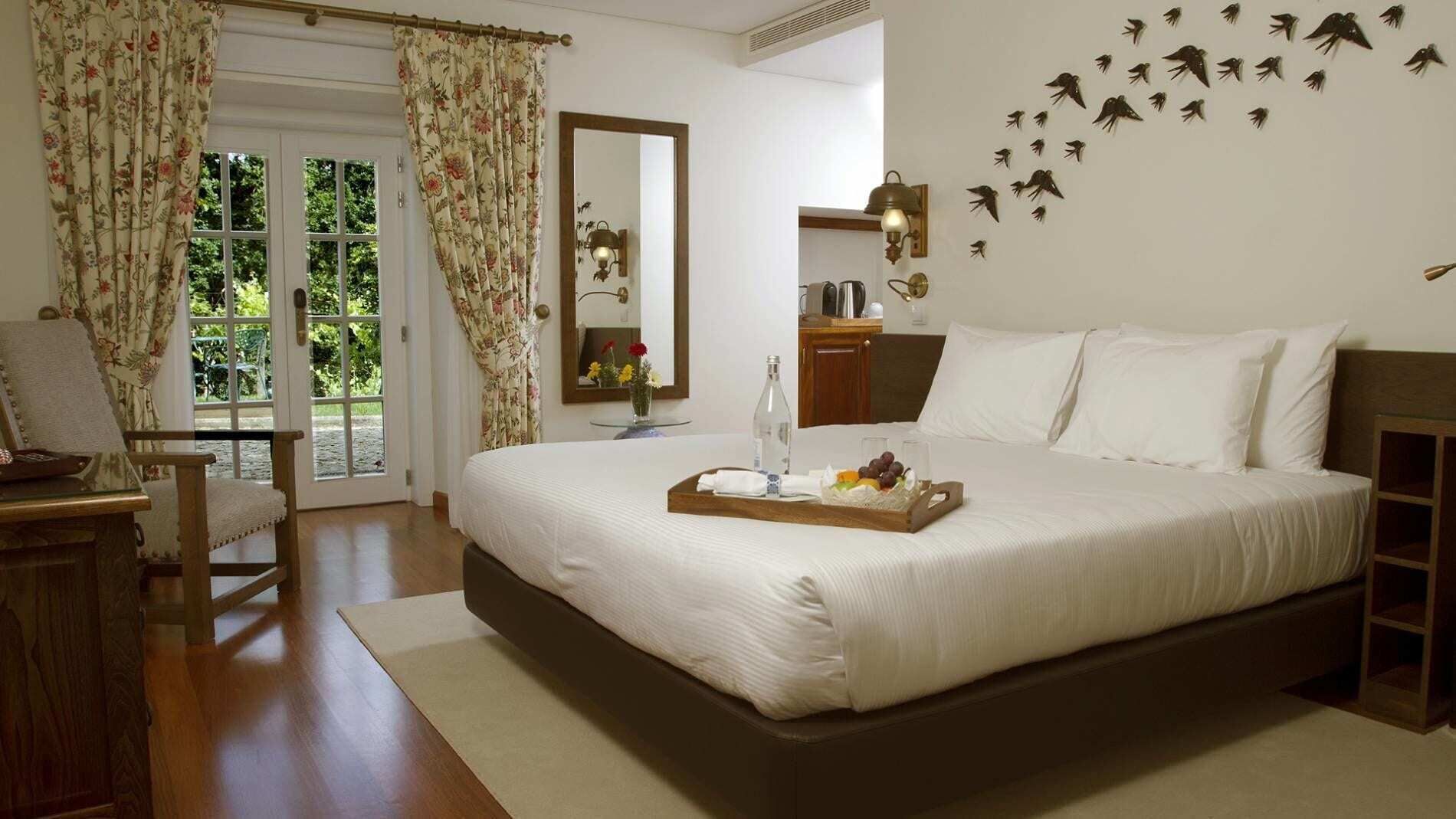 A bedroom with a large bed, a wooden nightstand, a chair, a desk, and a window with curtains.
