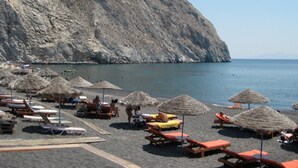 A beach with thatched umbrellas and wooden lounge chairs. - Anemolia Villa (Santorini)