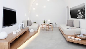 A modern living room with a large flat-screen TV, a sofa, a coffee table, and a dining table with chairs. - Anemolia Villa (Santorini)