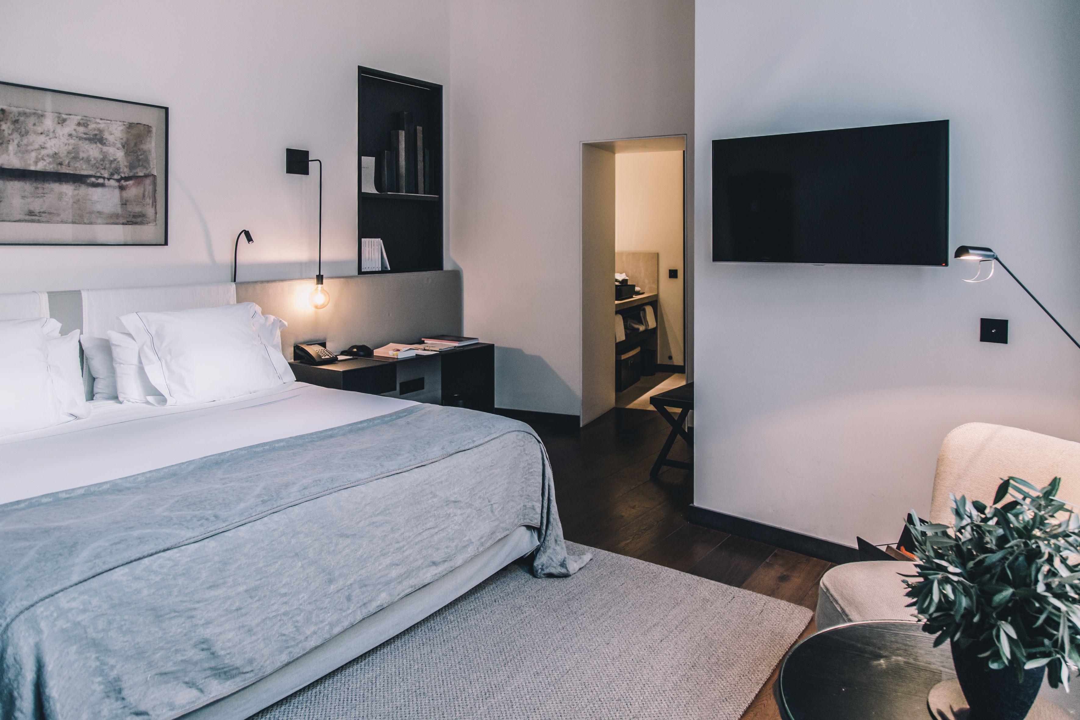 A modern hotel room with a large bed, a desk, a flat-screen TV, and a bookshelf.