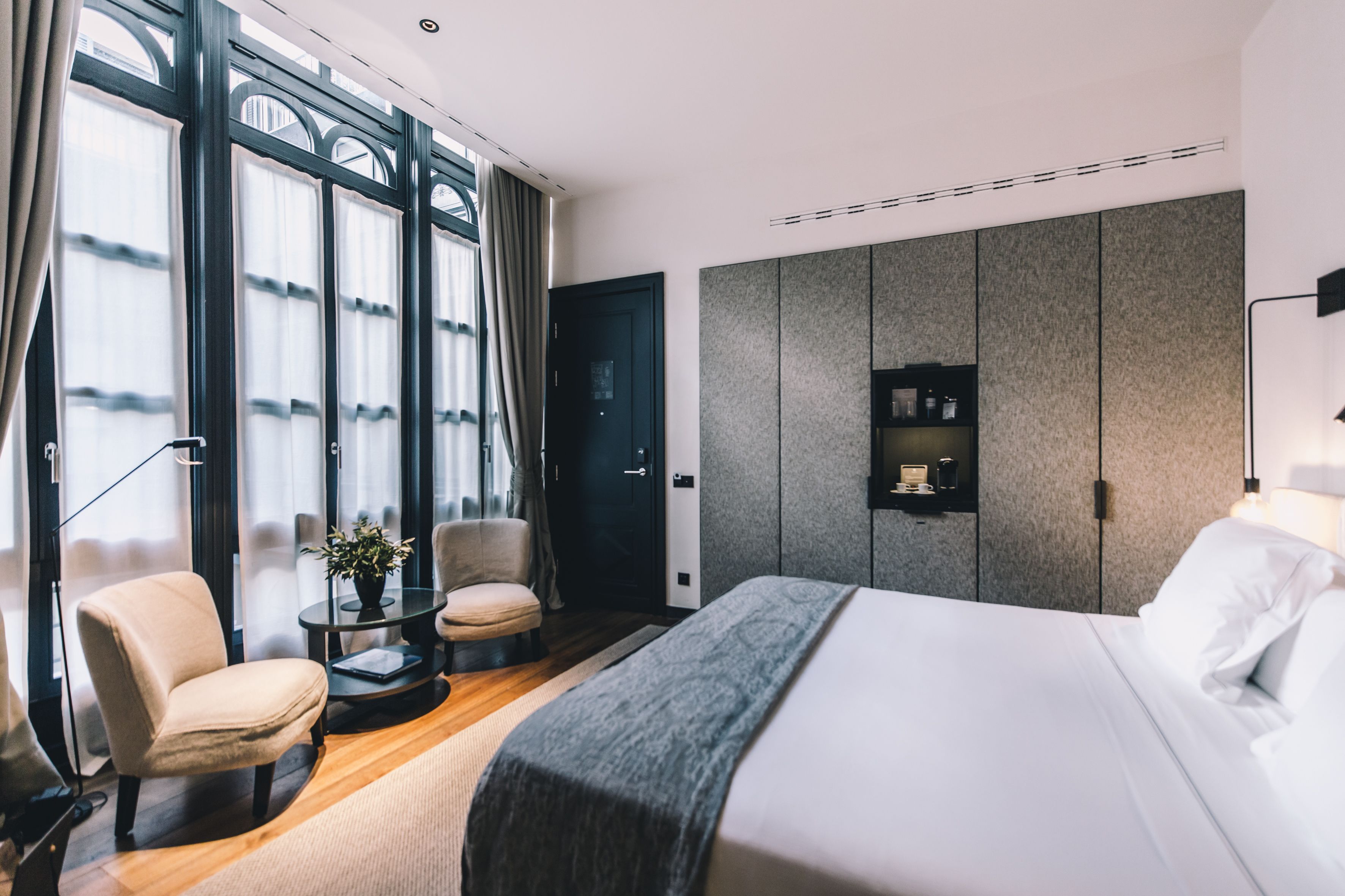 A modern hotel room with a large bed, two armchairs, a small table with a plant, and a wardrobe.