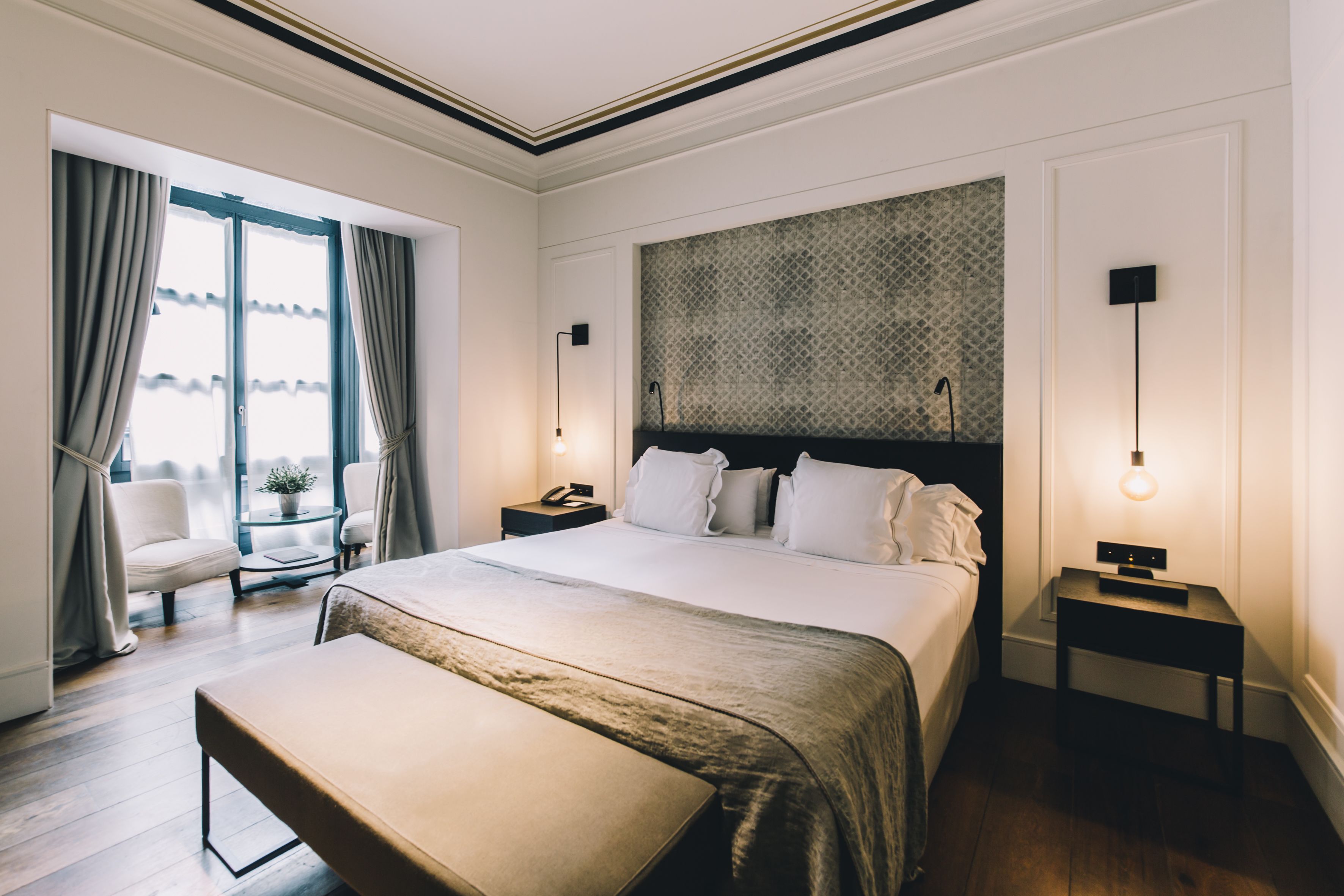 Habitación de hotel con una cama grande, un banco, un escritorio, una silla y vistas al exterior.