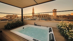 A rooftop terrace with a hot tub, wooden deck, and a view of historic buildings. - Sant Francesc Hotel Singular (Palma de Mallorca)