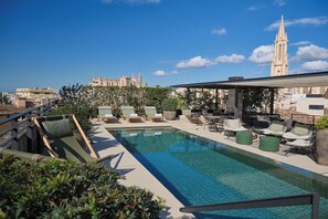 Une piscine sur le toit, dotée de chaises longues et offrant une vue sur un bâtiment historique en arrière-plan.