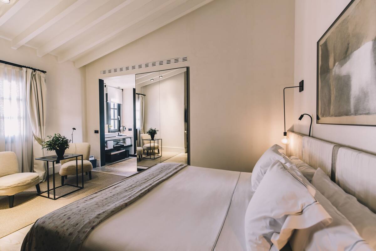 A modern bedroom with a large bed, a desk, a chair, and a mirror.