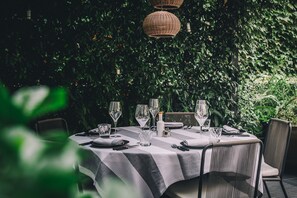 Une table dressée pour le dîner, recouverte d’une nappe blanche et entourée de chaises, dans un jardin luxuriant et verdoyant.