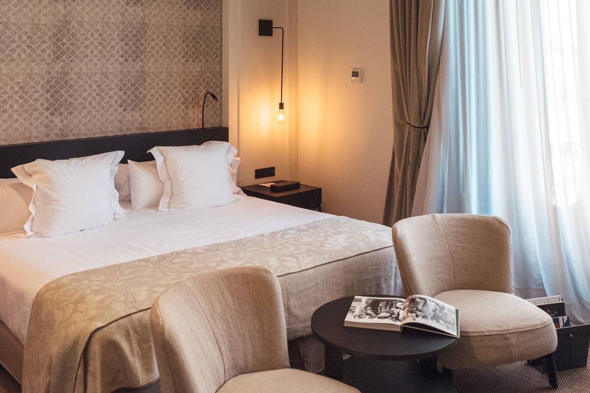 A hotel room with a large bed, two armchairs, a small round table, and a decorative ceiling.