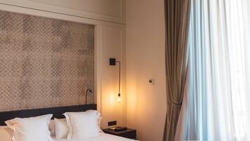 Habitación de hotel con una cama grande, dos sillones, una mesita redonda y un techo decorativo.