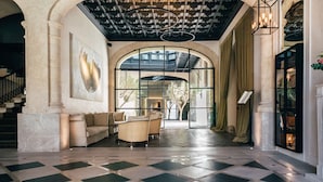 A spacious lobby with a checkered floor, a seating area with a sofa and chairs, and a large arched window with a view of the outdoors. - Sant Francesc Hotel Singular (Palma de Mallorca)