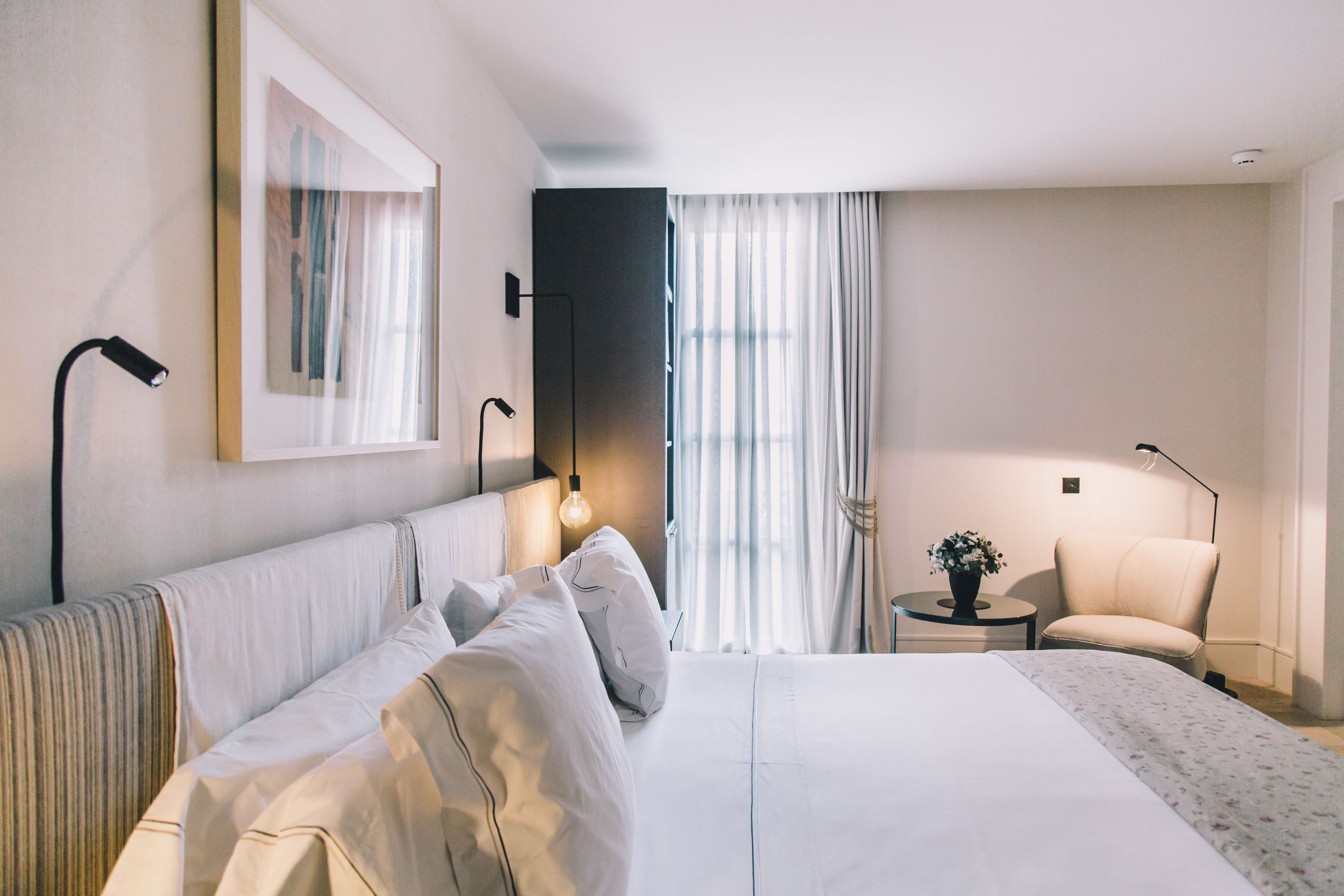 Une chambre d’hôtel avec un grand lit, une chaise, une petite table avec une plante et un miroir au mur.