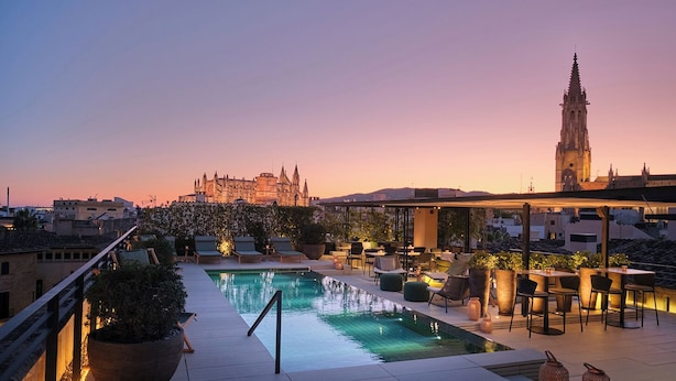 A rooftop pool area with lounge seating and a view of a historic building in the background. - Sant Francesc Hotel Singular (Palma de Mallorca)