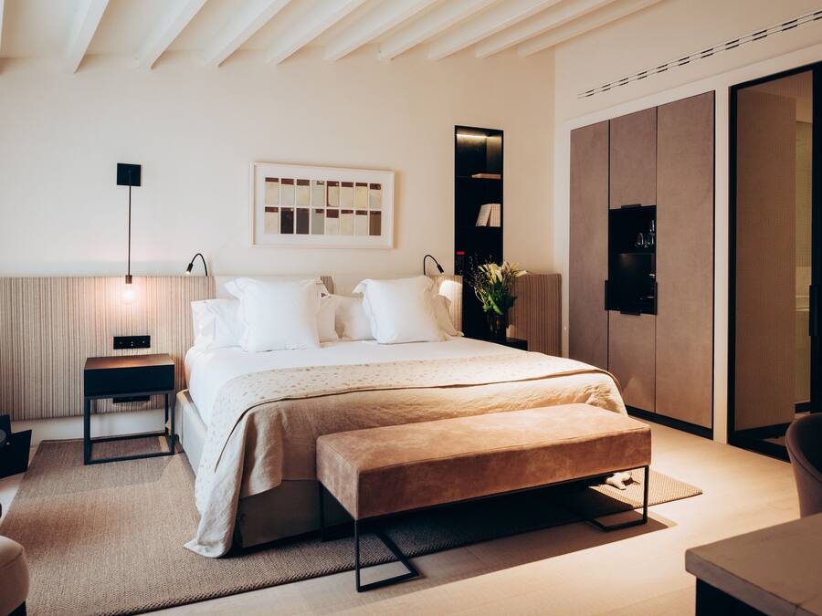 Un dormitorio moderno con una cama grande, mesitas de noche, una banca, un escritorio y un armario.