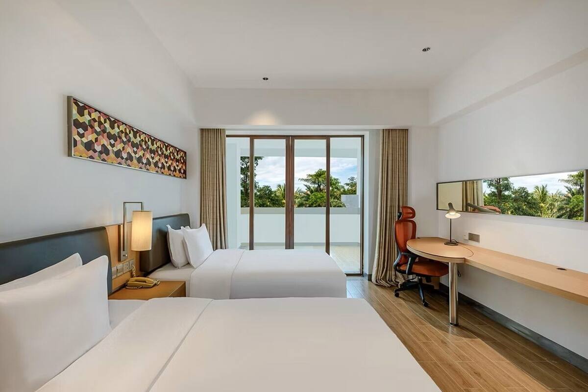 Habitación de hotel con dos camas, un escritorio, una silla, una lámpara, un ventanal grande y una luz en el techo.