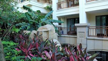 Un patio de hotel con abundante vegetación, una gran roca y una barandilla de piedra.