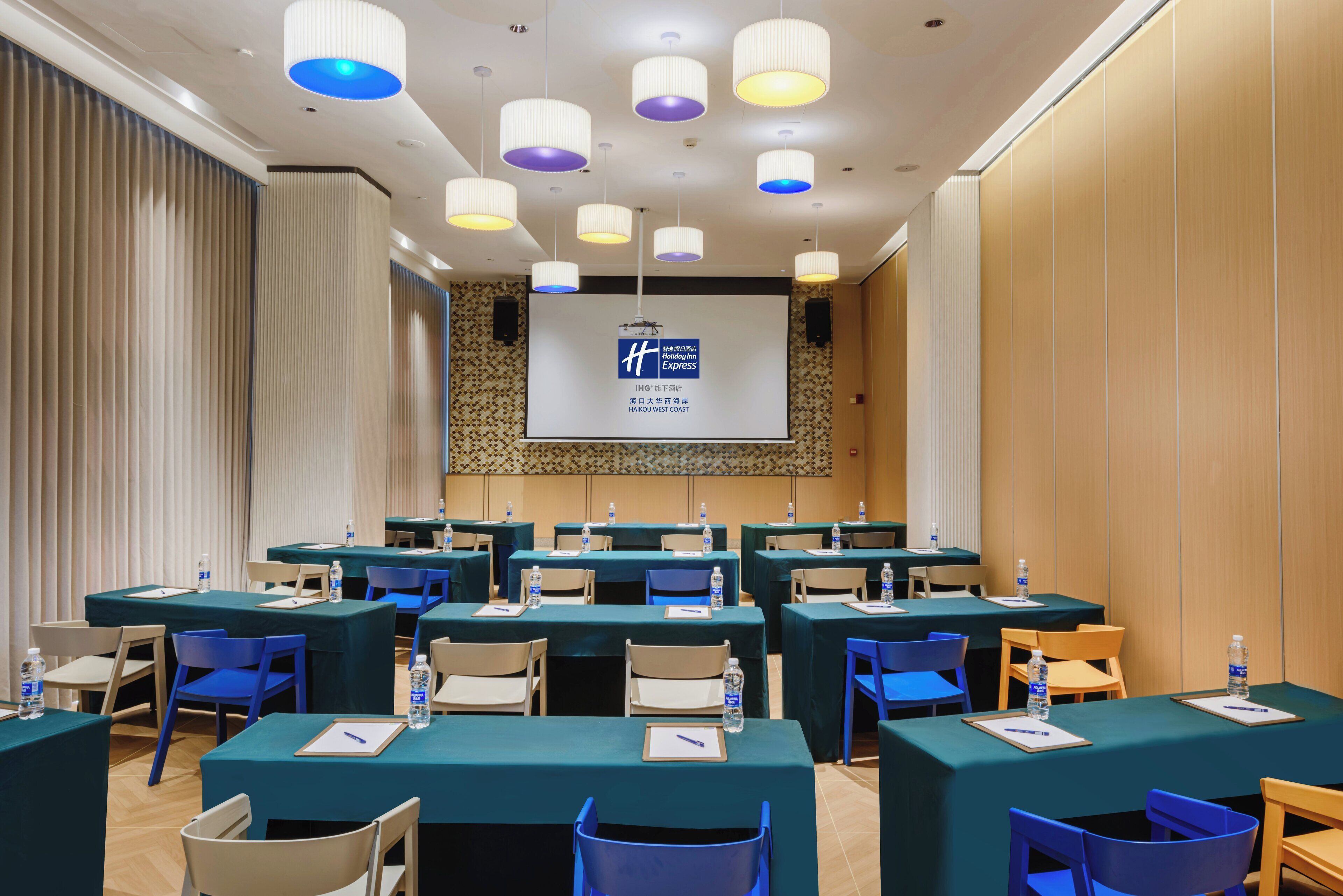 Un salón de conferencias con varias mesas, sillas y una pantalla de presentación.